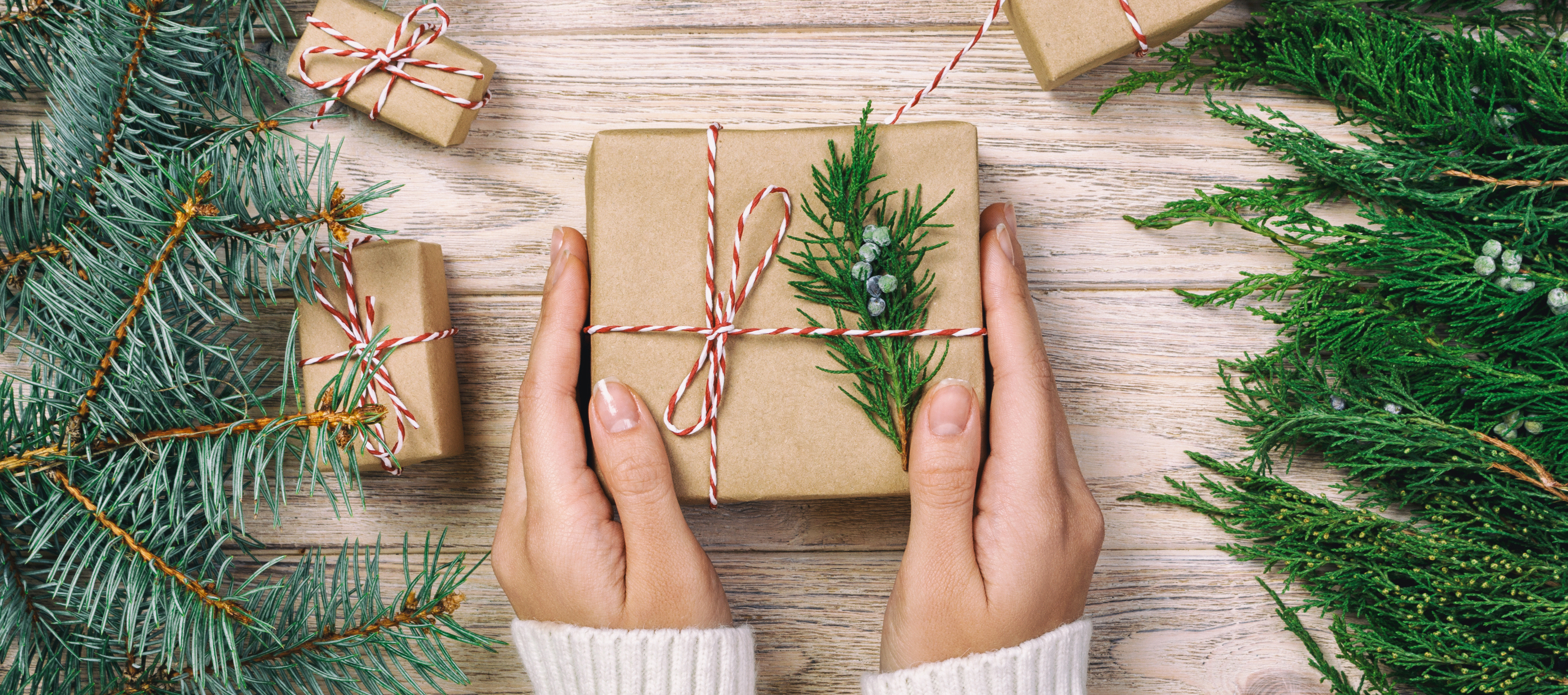 woman's hands holding a wrapped gift in a seasonal, holiday setting - Plan the Perfect Holiday Gift for Employees blog cover image