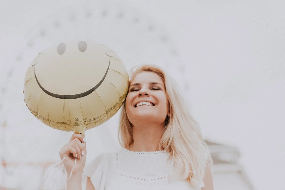 woman smiling holding a yellow smiley face balloon - relationship goals of marketing blog cover image 